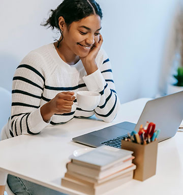 Lady drinking coffee while using her laptop computer